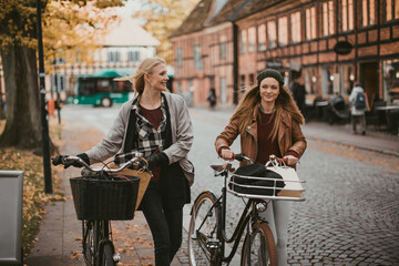 Naklejka premium Young lesbian couple riding bicycles together while shopping in the city