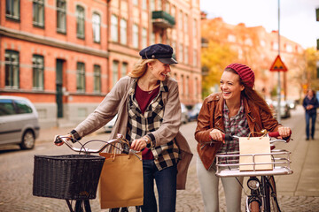 Two young female friends riding bikes while shopping in the city