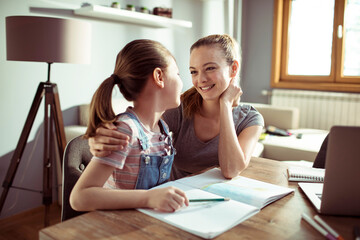 Young mother and daughter hugging in the living room while the daughter is drawing and coloring