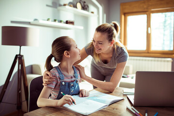 Obraz premium Young mother and daughter hugging in the living room while the daughter is drawing and coloring