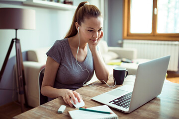 Fototapeta premium Young Caucasian woman studying and using her laptop at home
