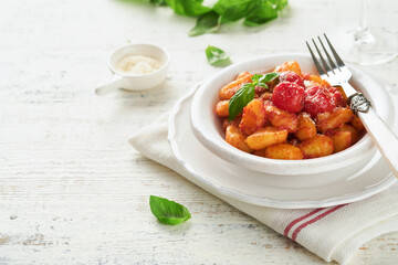 Potato gnocchi. Traditional homemade potato gnocchi with tomato sauce, basil and parmesan cheese on kitchen table on light grey kitchen table background. Traditional Italian food. Top view.