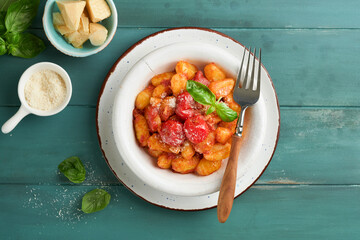 Potato gnocchi. Traditional homemade potato gnocchi with tomato sauce, basil and parmesan cheese on turquoise rustic kitchen table background. Traditional Italian food. Top view. - Powered by Adobe