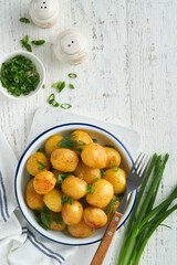 Boiled new or young potatoes with butter, fresh dill and onions in white bowl on white old rustic wooden background. Tasty new boiled potatoes. Top view.