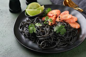 Black spaghetti pasta shrimp on black plate on dark concrete table background. Squid ink pasta with prawns. Pasta seafood. Top view on green stone table. Mediterranean traditional cuisine dish.