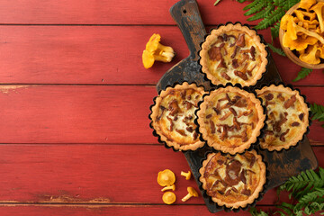 Savory hands pie with chanterelle mushrooms, cream and cheese on cutting board on rustic old red wooden table background. Homemade tarts with seasonal chanterelle mushrooms. Rustic style. Top view.