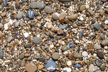 Oval stones on pebble beach, multicolored close-up, glare from the sun