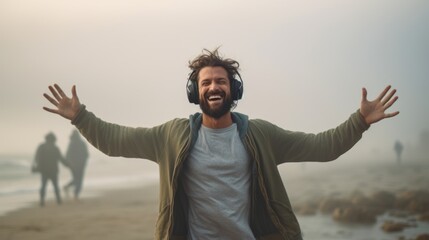 Inspired man dancing in headphones on foggy beach. Portrait of relaxed guy listening music in earphones. Male hipster making dance waves with hands. Dancer having fun. Entertainment leisure activity