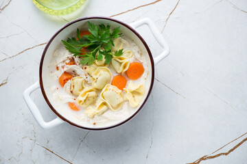 Bowl of creamy tortellini and chicken soup, flat lay on a white granite background, horizontal shot with space