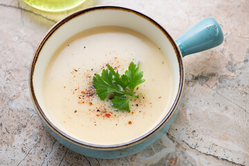 Cheese cream-soup in a turquoise serving bowl, horizontal shot on a pinkish granite background, middle close-up