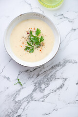 Bowl of cheese soup with fresh parsley on a light-grey marble background, vertical shot with space, above view