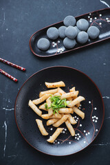Korean tteokbokki or rice cakes and mochi on a black marble background, vertical shot, top view