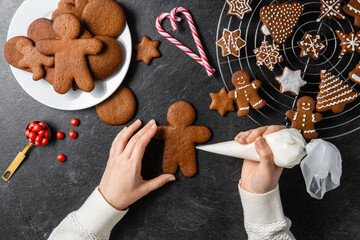 baking, cooking, christmas and food concept - close up of hands with pastry bag decorating gingerbread cookies with white icing on black table top