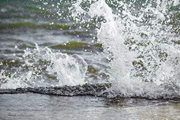 Splashes from breaking sea surf about the concrete pier, close-up, selective focus