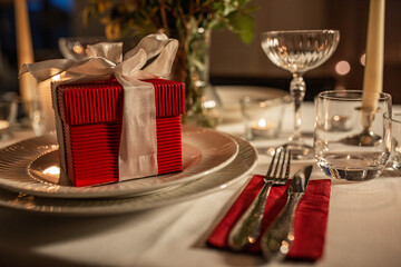 holidays, dinner party and celebration concept - close up of festive table serving with gift box, flowers in vase and candles burning at home on valentine's day