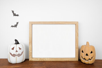 Halloween mock up. Wooden frame on a wood shelf with jack o lantern decor. Landscape frame against a white wall. Copy space.