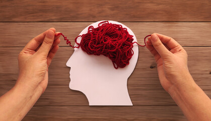 Mental health and problems with memory. Hands unraveling tangled red threads on head silhouette representing brain.