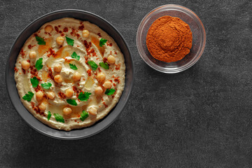 Hummus with oil and spices in gray bowl, on slate stone plate round, dark background, top view
