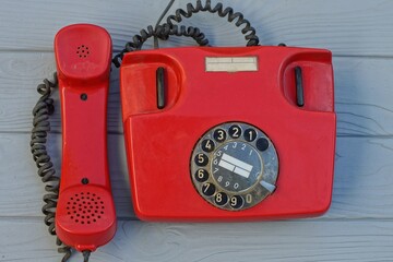 landline, rotary with dialer plastic old classic red office with black wire telephone with the receiver on-hook standing on a gray wooden table - obrazy, fototapety, plakaty