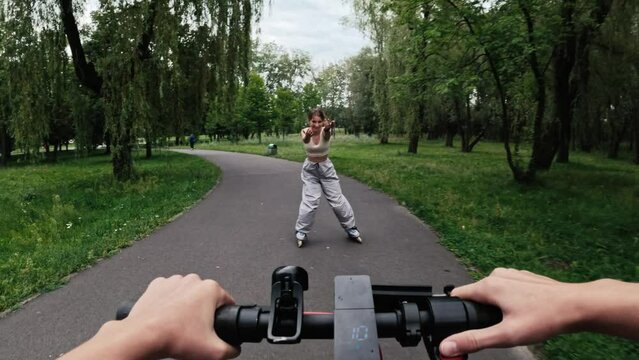 Young woman riding electric scooter with rollerscating teenager girl in park. Friends with modern vehicles enjoying nature outdoors activities