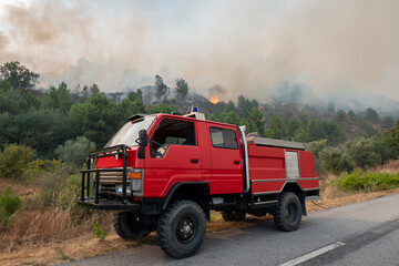 Viatura dos bombeiros junto à estrada na luta de um incêndio florestal com grandes labaredas que vão deixando uma grande nuvem de fumo no ar