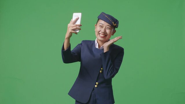 Asian Woman Air Hostess Using Smartphone Taking Picture While Standing In The Green Screen Background Studio
