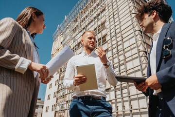 Young construction engineers discussing new project together standing in a construction site