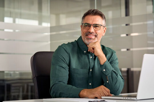 Happy Mature Business Man Of Middle Age, Confident Entrepreneur Or Bank Manager, 45 Years Old Executive, Mid Aged Businessman Investor Sitting At Work Desk In Office Looking Aside. Copy Space.