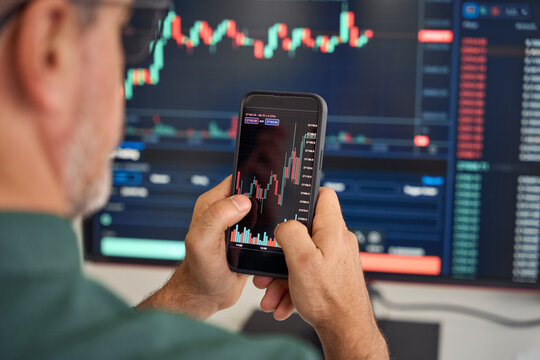 Investor trader broker analyzing financial crypto stock trade market on smartphone risk digital price data in mobile app buying bank shares, doing investment strategy analysis on phone. Over shoulder. - Powered by Adobe