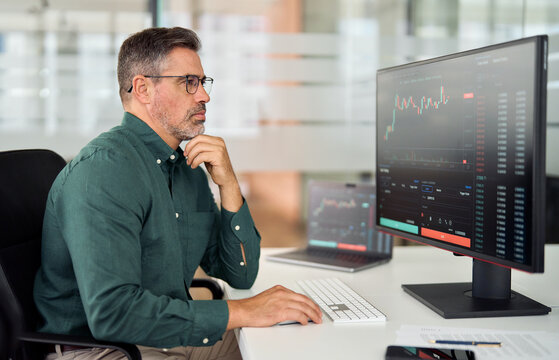 Middle aged busy business man crypto broker, financial investor, stock trader analyzing online market price growth thinking of investing strategy in digital trading exchange working in office.