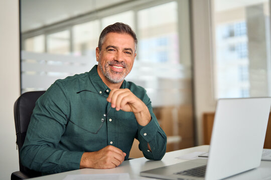 Happy Smiling Indian Older Business Man, Middle Aged Professional Businessman Ceo Executive Bank Manager, Mature Investor Sitting At Work Desk In Office With Laptop Looking At Camera, Portrait.