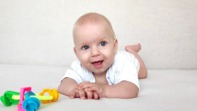 Funny baby laughs and plays with a rattle on a white blanket, baby's morning