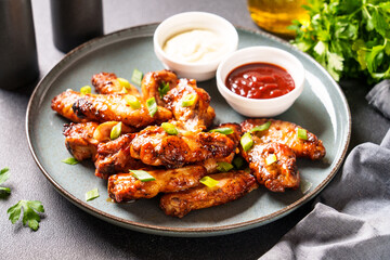 Chicken wings in bbq sauce. Grilled meat with two sauces at craft plate.