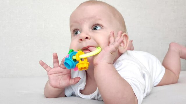 Funny baby laughs and plays with a rattle on a white blanket, baby's morning