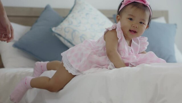 an Asian baby joyfully crawls out of bed, cheered on by a mother.