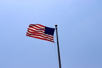 The US flag waving in the wind with a clear sky background.