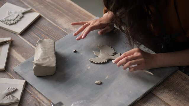 Young woman hands in pottery studio using pottery tools creating a dove, handmade ceramics, creative. Pretty girl work as a ceramist. Closeup of creative process, work on details. Hobby design concept