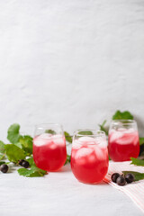 Three Glasses of Muscadine Lemonade with Muscadines and Vines in the Background on a White Surface