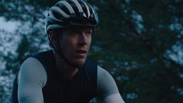 Portrait of professional road cyclist in lightweight helmet in tight fitting lycra jersey ride on carbon bike in cinematic light. Hard cardio training during off season