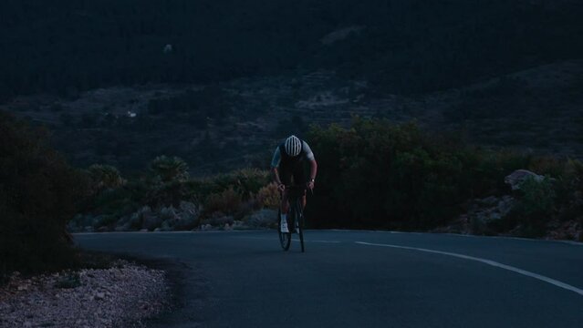Slow motion gimbal shot of professional road cyclist on carbon bike climb steep mountain hill interval during cardio training. Perform hard effort to achieve success and win