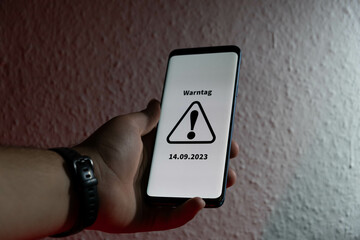 Symbol for the national warning day in Germany, 2022. Hand holds a mobile phone with the German text "Warntag 8. Dezember" (warning day on December 8th).