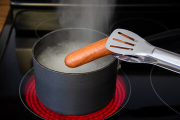 Tongs holding boiled hot dog