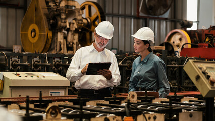 Factory engineer manager with assistant using laptop to conduct inspection of steel industrial machine, exemplifying leadership as machinery engineering inspection supervisor in metalwork manufacture.