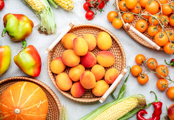 Fall colorful vegetables and fruits set: apricots, tomatoes, paprika, pumpkin, corn, etc. in wicker trays on rustic linen background, top view