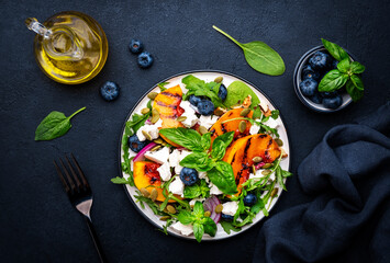 Gourmet salad with grilled peaches, blueberries, red onion, feta cheese, basil and mixed herbs, black table background, top view
