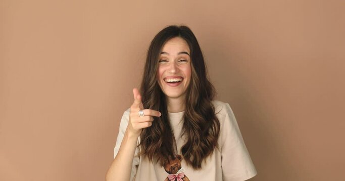 Young excited cheerful funny brunette woman look camera laugh smiling watch comedy movie, listening joke, pointing index finger on you isolated on beige background studio portrait.