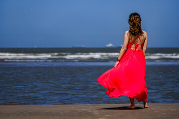 Fototapeta na wymiar Beautiful Woman Walking on Beach with Red Dress, Long Hair, and Fashionable Hairstyle