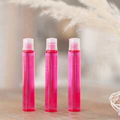 a set of three tall pink small jars standing on a wooden table with dried flowers in the background