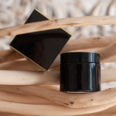 black jar for cream and its box on a background of wooden branches