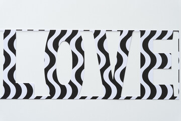 the word "love" cut from paper with wavy black and white lines on blank paper